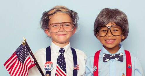 Two children holding flags and signs encouraging others to vote