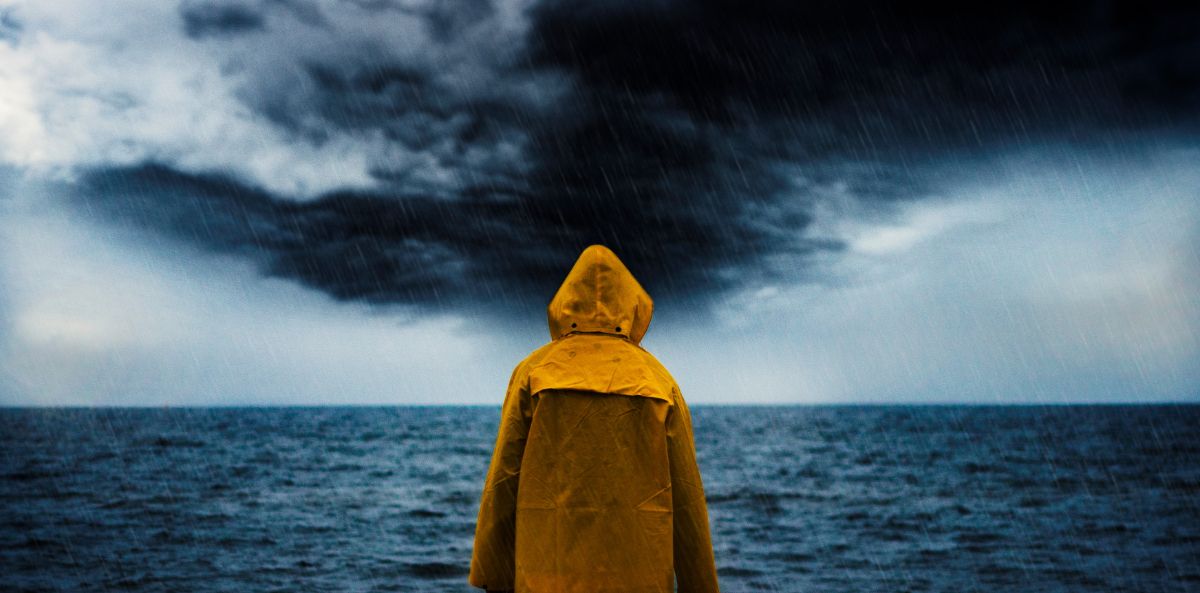 A man in a yellow coat staring at the Sea and a dark sky