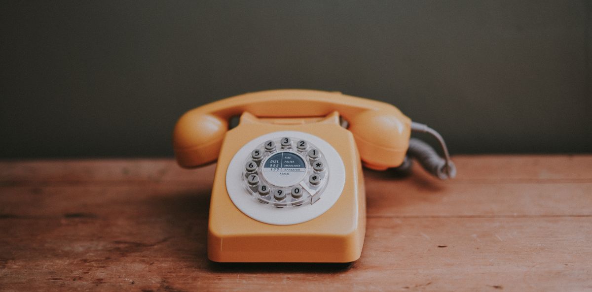internal communications - orange rotary phone on wooden table and green wall background.