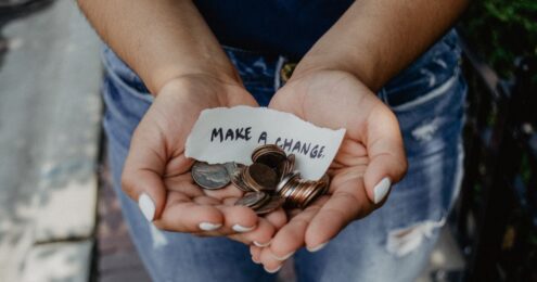 A person holding with both hands together cents, quarters, nickels and dimes along with a piece of paper that says Make A Change