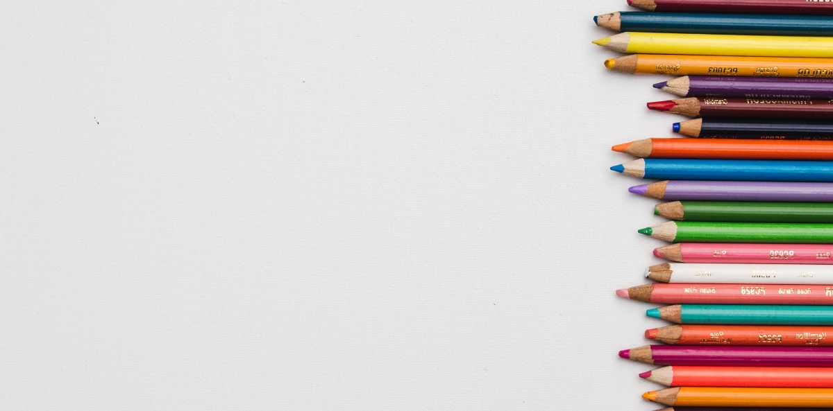 A picture of an assortment of colored pencils lined up sideways on the right hand side of a grey background.
