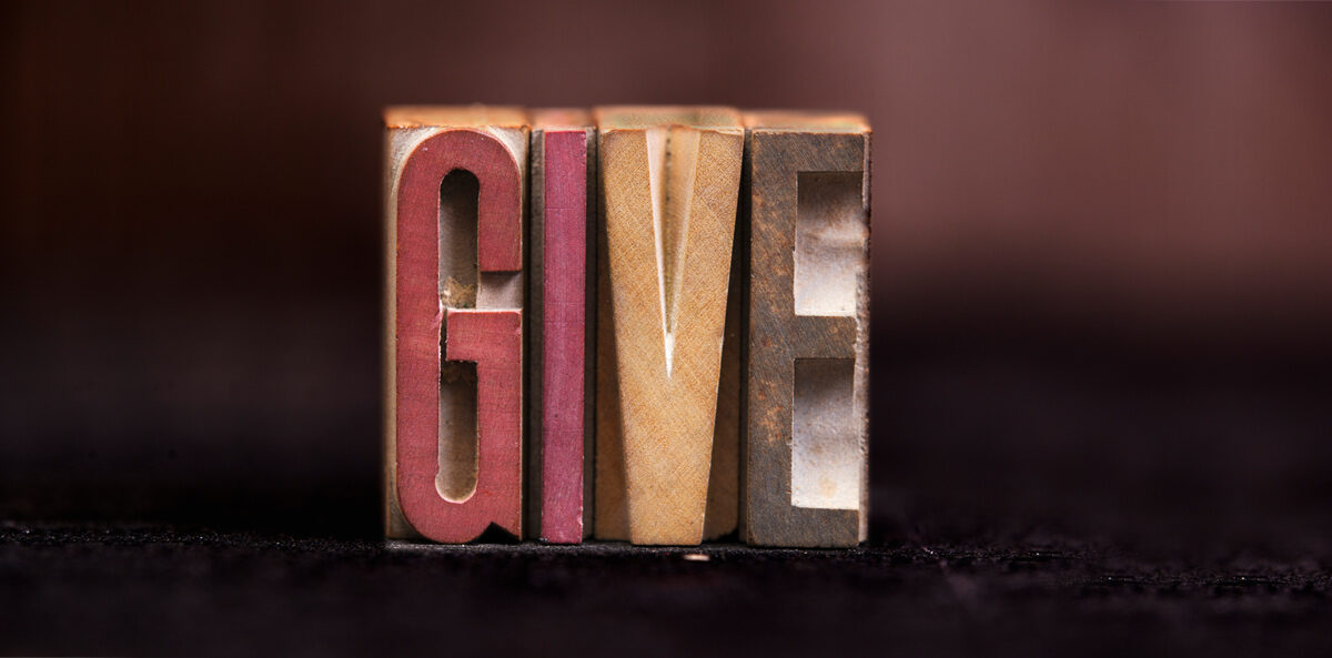 nonprofit board giving policy - give spelled out on different colored wooden blocks. The G is a red color. The I is a mauve color. The V is a yellow color. The E is a grey color.