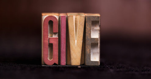 nonprofit board giving policy - give spelled out on different colored wooden blocks. The G is a red color. The I is a mauve color. The V is a yellow color. The E is a grey color.
