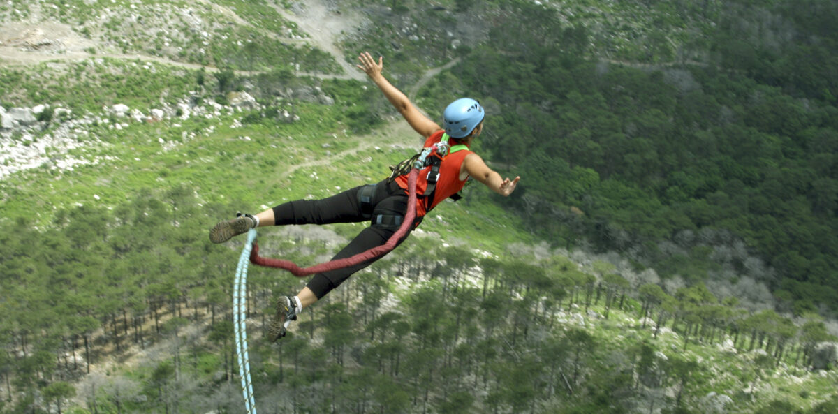 nonprofit executive director - a woman with tanned skin is jumping out over a landscape with trees attached to a bungee cord