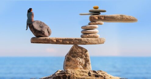 image of large rocks arranged like a scale with a woman sitting on the leftmost part of the rock and a stack of ore rocks on the right side of the rock scale making the two sides level.
