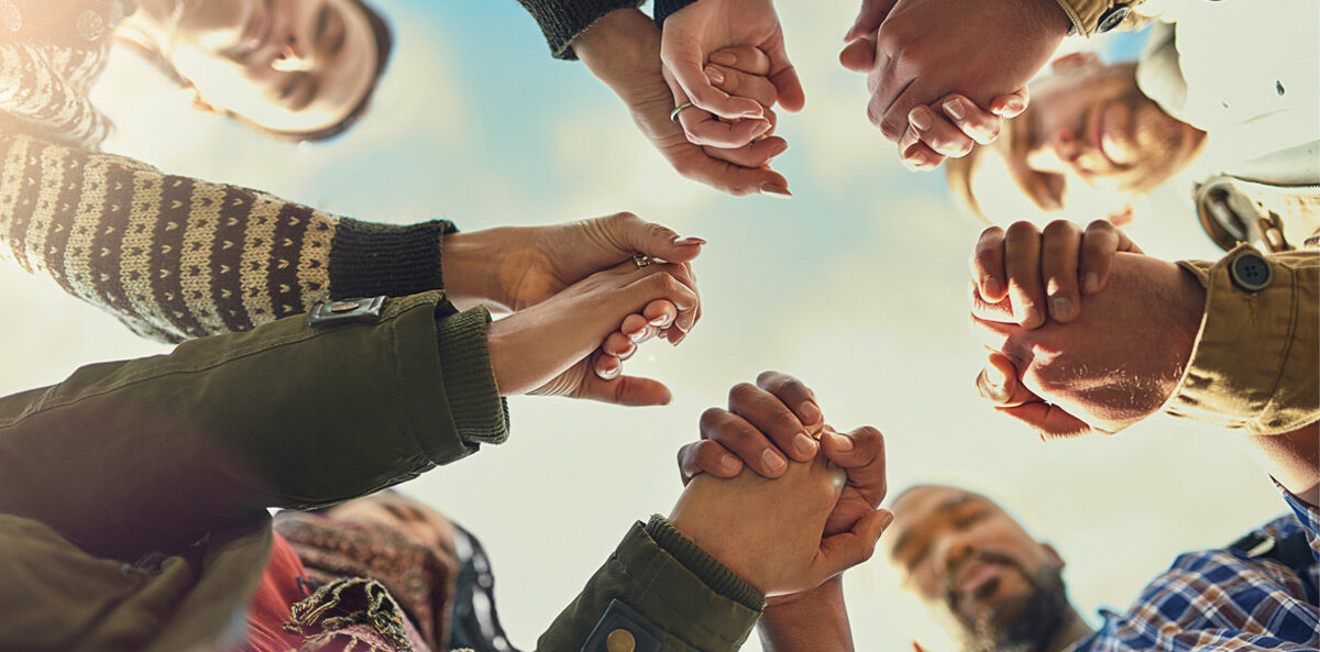 leadership team - Five pairs of hands holding the hand next to it reaching over the camera belonging to people of different races and genders.