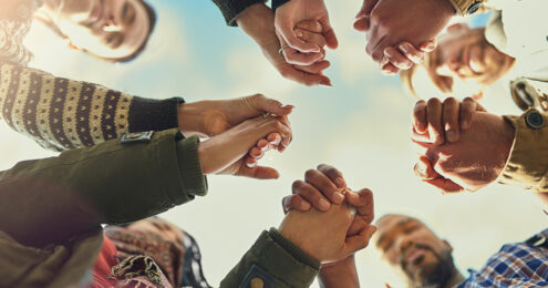 leadership team - Five pairs of hands holding the hand next to it reaching over the camera belonging to people of different races and genders.
