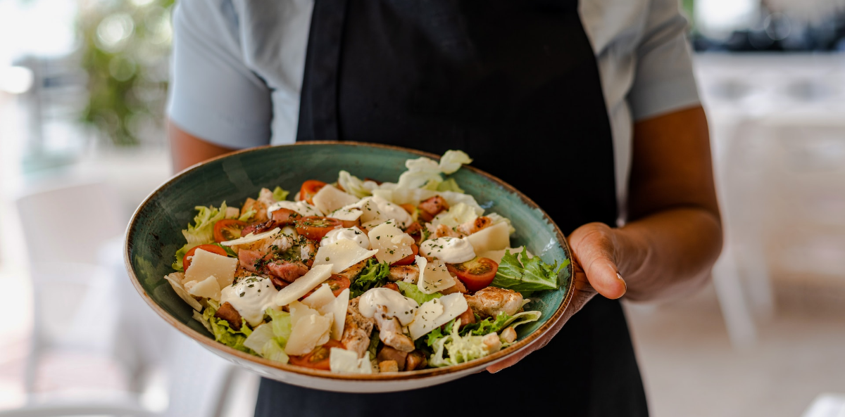 Picture of a chef holding a bowl of a colorful pasta salad. Represents a lunch date for a fervent fundraiser.
