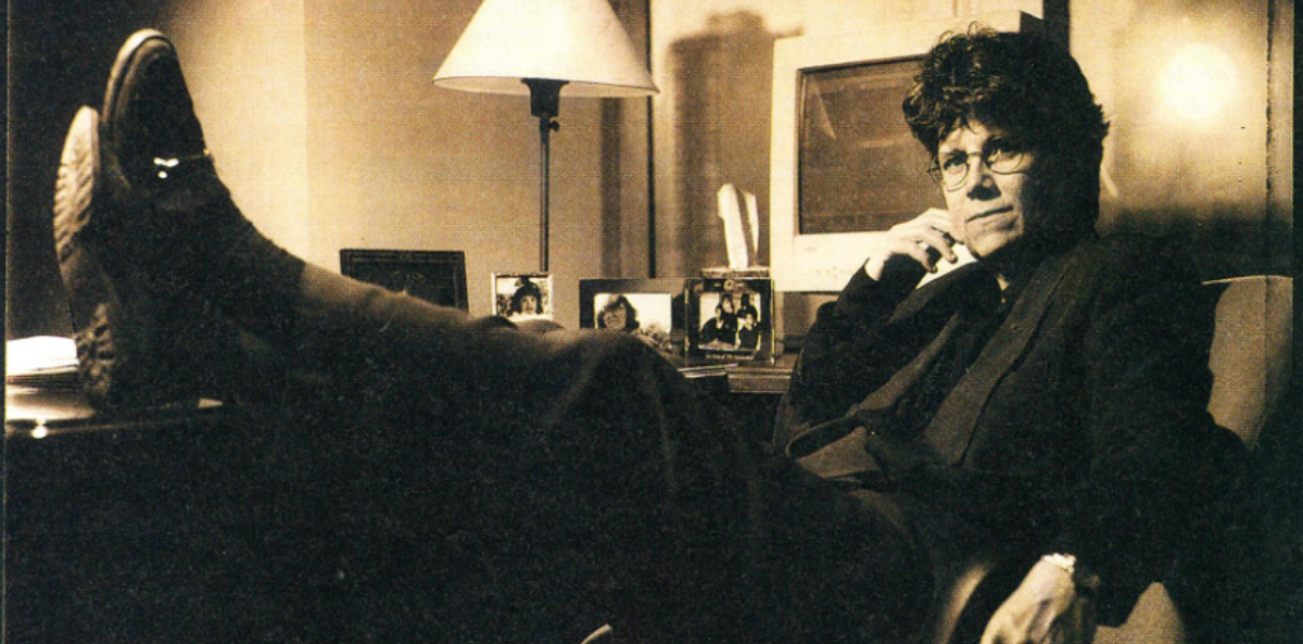 Joan Garry, at age 39, sits with her feet up on a desk, looking at the camera.