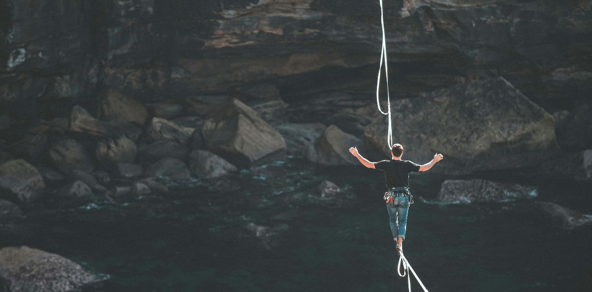 A woman walks a high-wire over a dark canyon with arms spread wide. She must balance herself to survive.